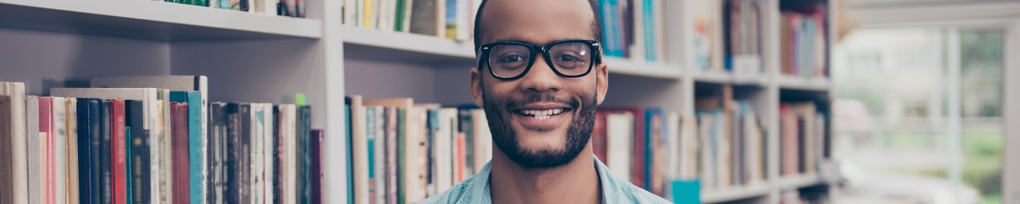 Retrato de um jovem estudante segurando livros na sala de arquivo da biblioteca da faculdade com muitos livros nas prateleiras